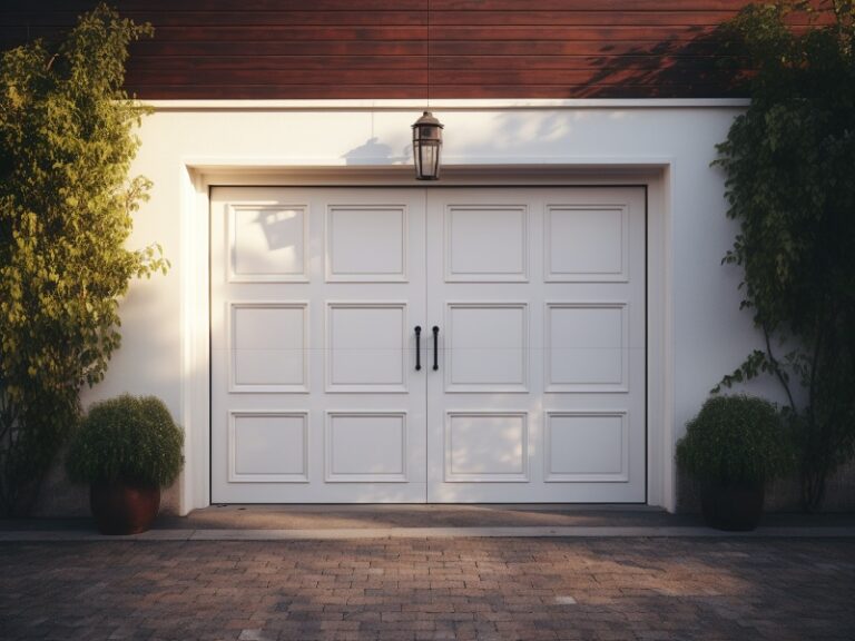 A white double garage door with decorative handles, flanked by potted plants and illuminated by a wall lantern.